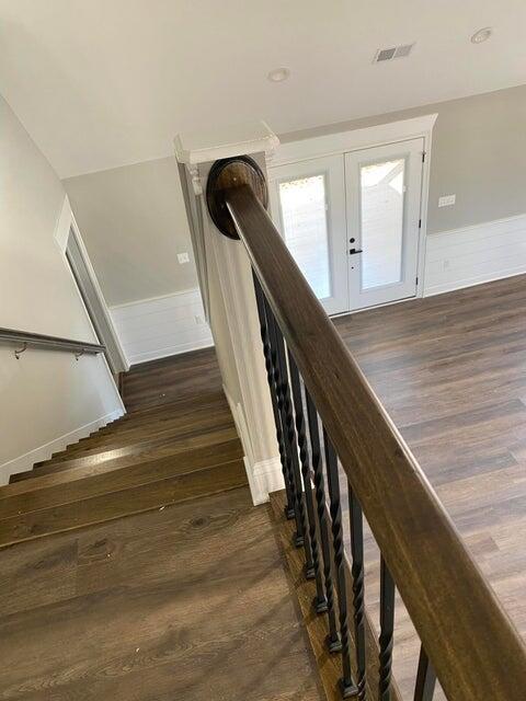 staircase featuring french doors, a wainscoted wall, visible vents, and wood finished floors