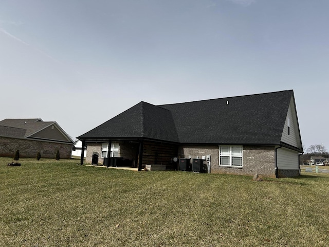 rear view of house with a shingled roof, brick siding, a yard, and central AC