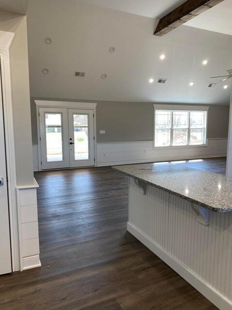 kitchen with vaulted ceiling with beams, light stone countertops, a kitchen bar, and dark wood finished floors