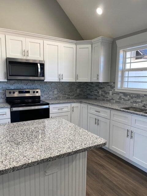 kitchen featuring white cabinets, appliances with stainless steel finishes, vaulted ceiling, and dark wood-type flooring