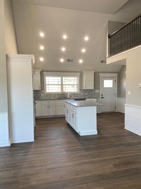 kitchen featuring a high ceiling, white cabinets, wainscoting, a center island, and dark wood-style floors