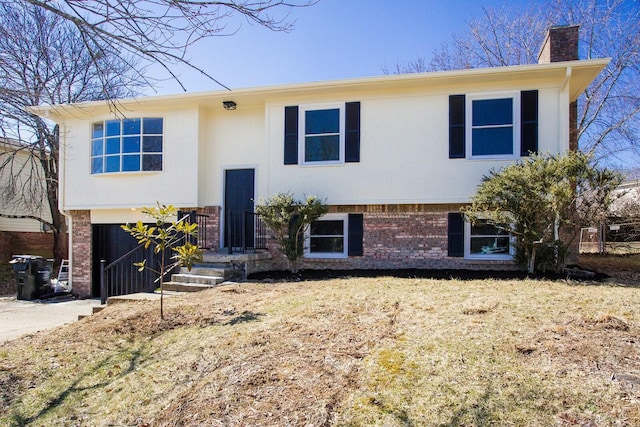 raised ranch with concrete driveway, brick siding, a chimney, and an attached garage