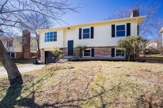 split foyer home with an attached garage, a chimney, concrete driveway, and brick siding