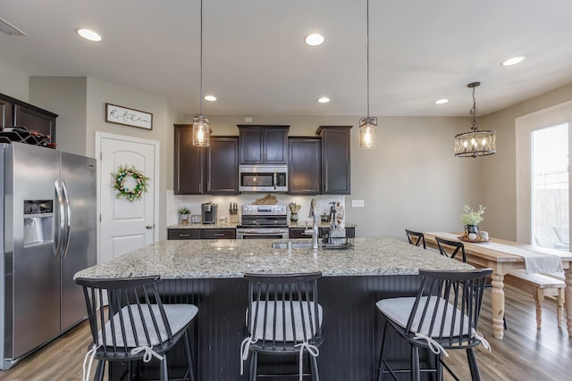 kitchen with a sink, light wood-style floors, appliances with stainless steel finishes, and light stone counters