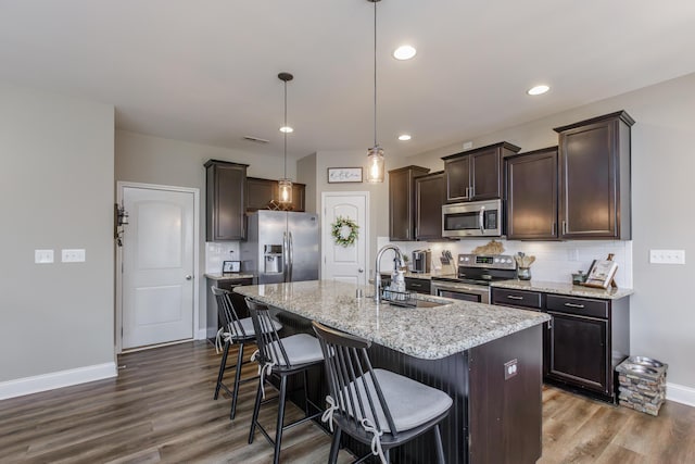 kitchen with dark brown cabinetry, a sink, appliances with stainless steel finishes, dark wood-style floors, and tasteful backsplash