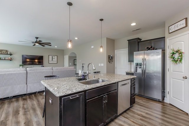 kitchen featuring arched walkways, stainless steel appliances, a sink, light wood-type flooring, and an island with sink