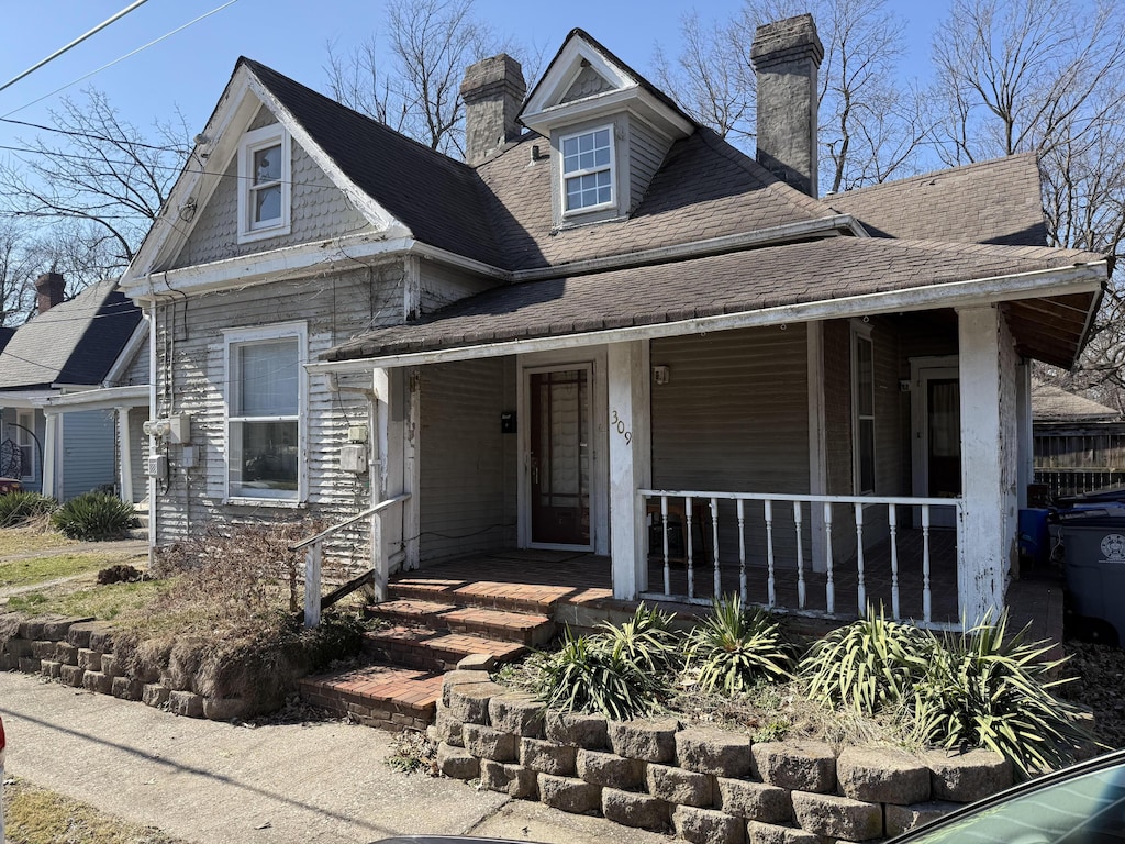 view of front facade featuring covered porch, a shingled roof, and a chimney