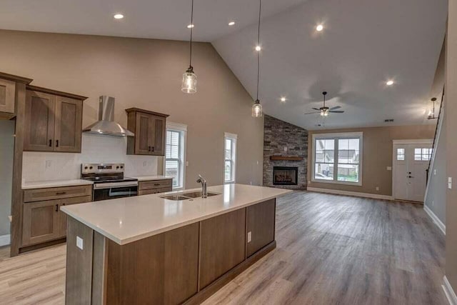 kitchen with light wood finished floors, light countertops, a sink, stainless steel range with electric stovetop, and wall chimney exhaust hood