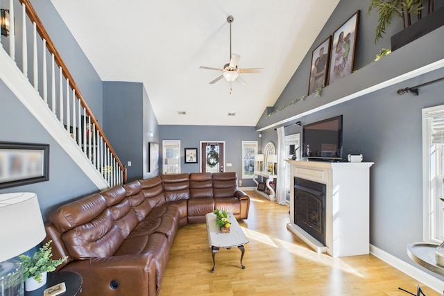 living area featuring a glass covered fireplace, stairway, wood finished floors, and ceiling fan