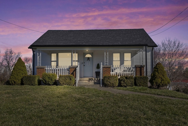 bungalow with brick siding, covered porch, a front lawn, and roof with shingles