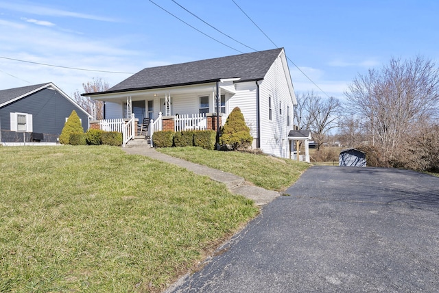 bungalow-style house with aphalt driveway, covered porch, a front lawn, and a shingled roof