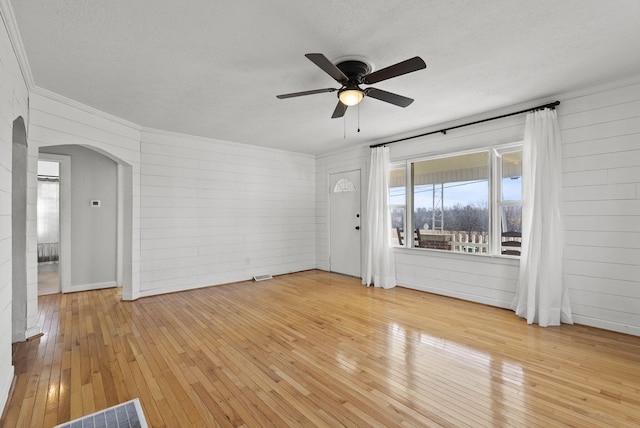 interior space with visible vents, a textured ceiling, arched walkways, light wood finished floors, and ceiling fan