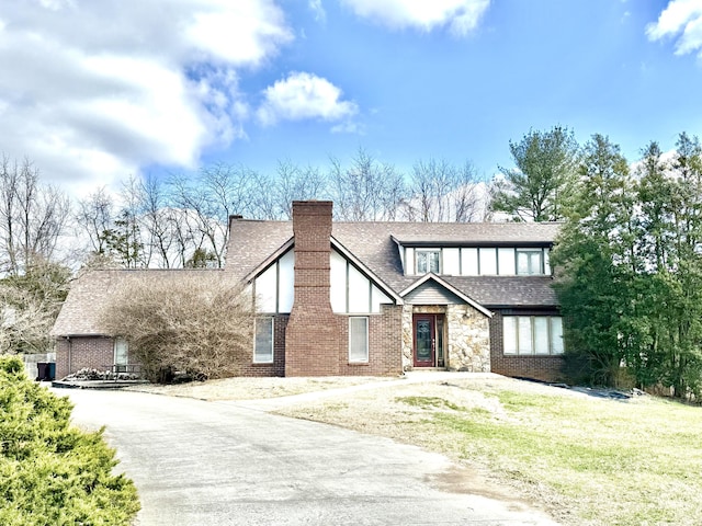 tudor house with brick siding, roof with shingles, stucco siding, a chimney, and a front yard