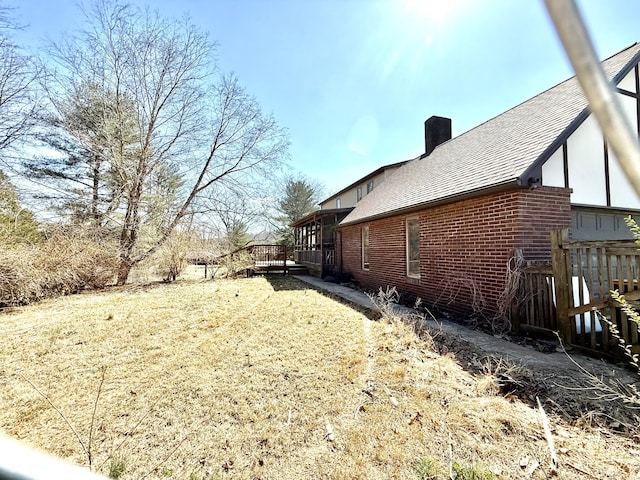 view of property exterior with a shingled roof, brick siding, a chimney, and a wooden deck