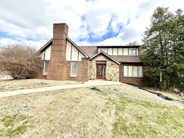 english style home with stone siding, roof with shingles, brick siding, and a chimney