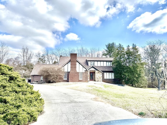 tudor home featuring a shingled roof, stone siding, a chimney, and a front lawn