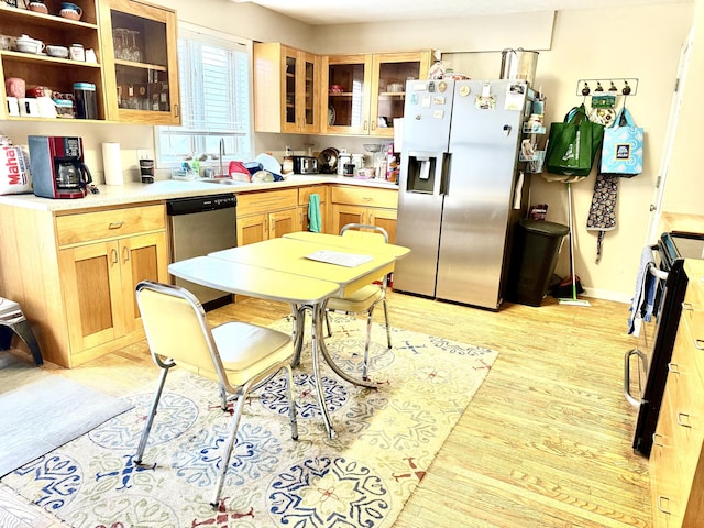 kitchen featuring light wood finished floors, glass insert cabinets, stainless steel appliances, light brown cabinetry, and a sink