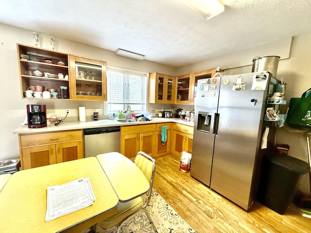 kitchen featuring light wood-style flooring, a sink, light countertops, appliances with stainless steel finishes, and glass insert cabinets