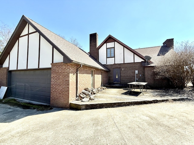 exterior space with brick siding, a chimney, roof with shingles, an attached garage, and stucco siding