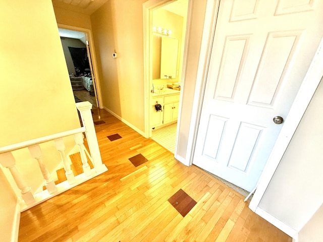 corridor with light wood-style floors, baseboards, and an upstairs landing