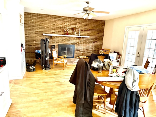 dining space featuring a ceiling fan, brick wall, wood finished floors, french doors, and a brick fireplace