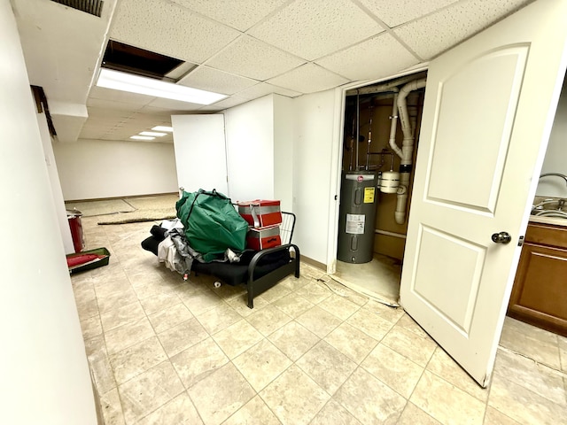 finished below grade area with baseboards, electric water heater, a drop ceiling, and light tile patterned floors