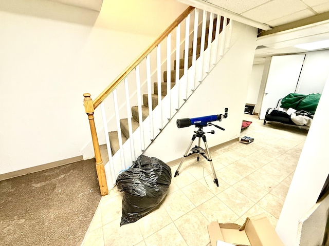 staircase with tile patterned flooring, a paneled ceiling, and baseboards