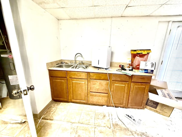 kitchen featuring brown cabinetry, a drop ceiling, light countertops, water heater, and a sink