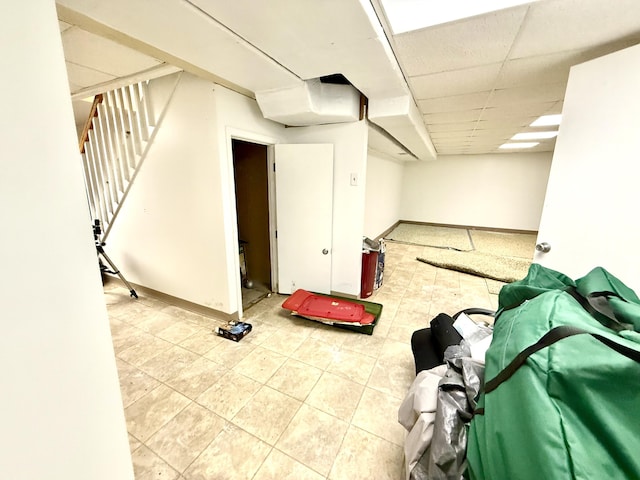 finished below grade area featuring a paneled ceiling, stairs, and baseboards