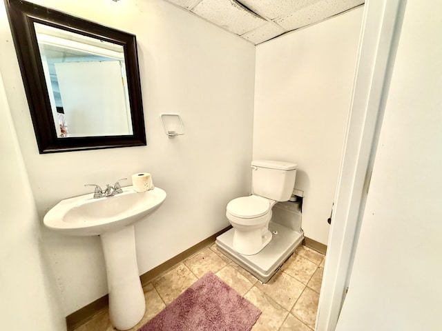 bathroom with a paneled ceiling, toilet, a sink, baseboards, and tile patterned floors