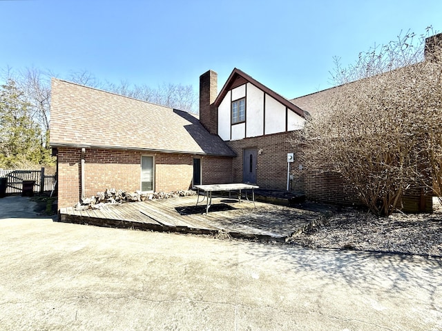 back of property with a shingled roof, a chimney, fence, a wooden deck, and brick siding