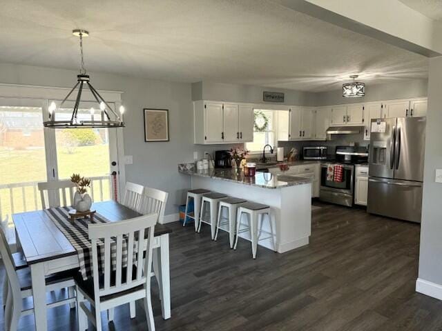 kitchen featuring a peninsula, under cabinet range hood, appliances with stainless steel finishes, and white cabinets