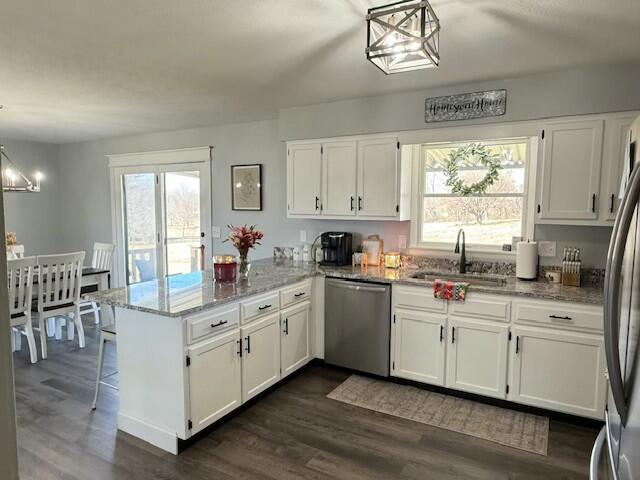 kitchen featuring stainless steel appliances, a peninsula, a sink, and white cabinetry