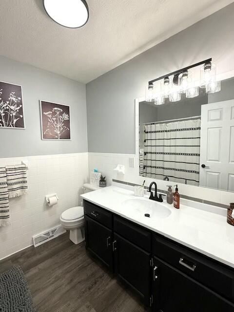 full bathroom featuring a textured ceiling, toilet, wood finished floors, vanity, and visible vents