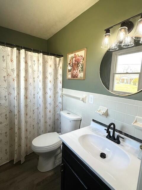 bathroom with toilet, a wainscoted wall, wood finished floors, vanity, and tile walls