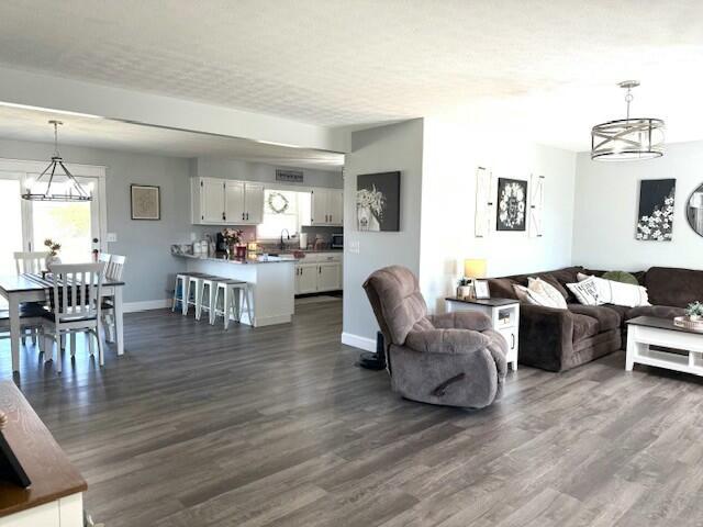 living room with dark wood-style floors, baseboards, and an inviting chandelier