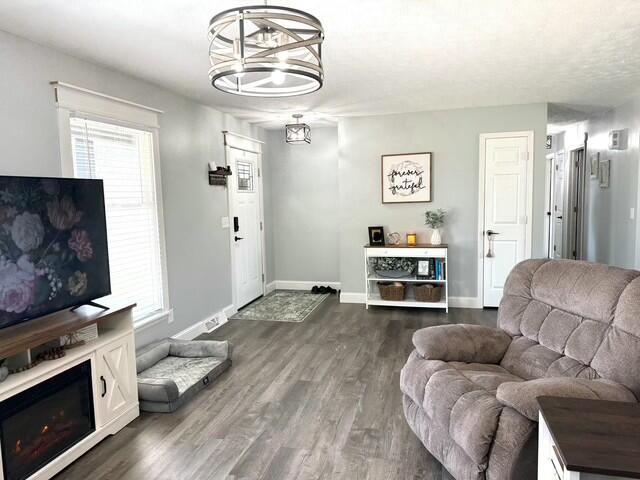 living area with dark wood-style floors, a chandelier, a lit fireplace, and baseboards