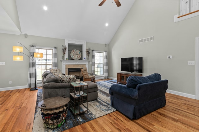 living room featuring visible vents, high vaulted ceiling, a large fireplace, light wood finished floors, and baseboards