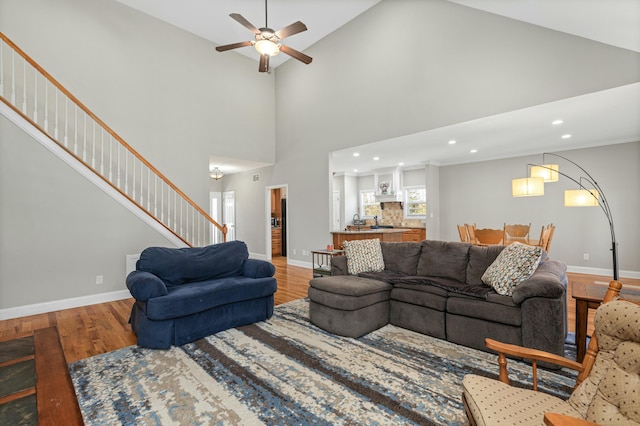 living area featuring high vaulted ceiling, a ceiling fan, wood finished floors, stairway, and baseboards