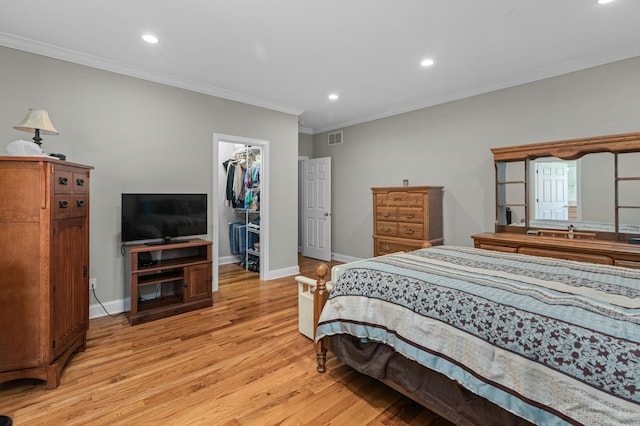 bedroom with a walk in closet, crown molding, visible vents, and light wood-type flooring