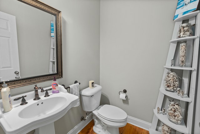 half bathroom with wood finished floors, toilet, baseboards, and a sink