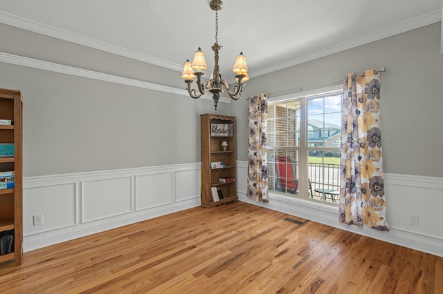 unfurnished room with visible vents, ornamental molding, wainscoting, light wood-style flooring, and an inviting chandelier