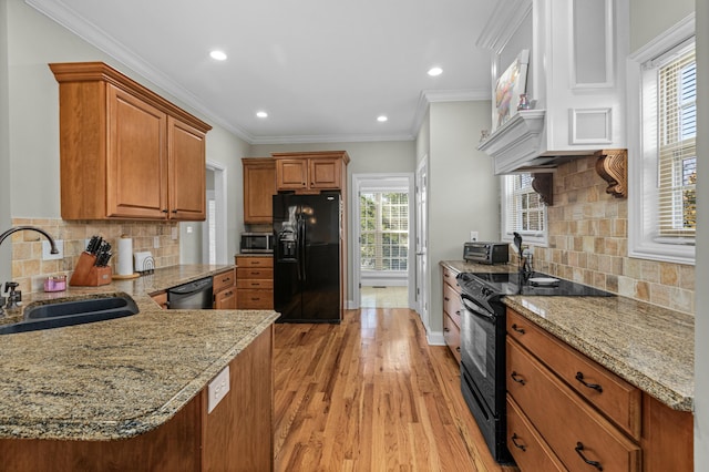 kitchen with a sink, light wood-type flooring, light stone countertops, and black appliances