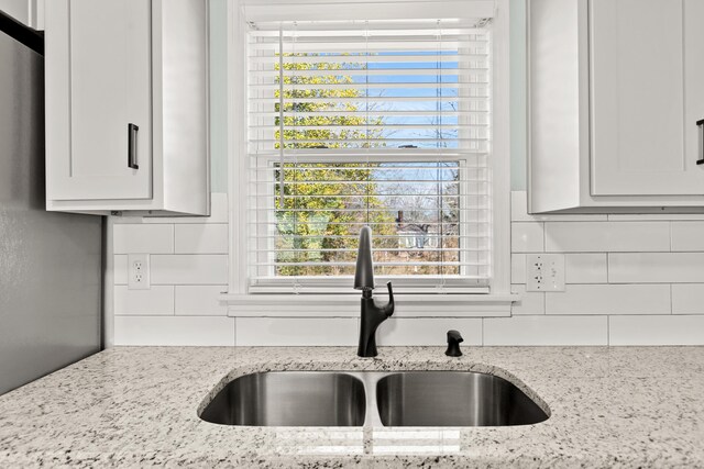 kitchen featuring a sink, light stone counters, backsplash, and white cabinetry