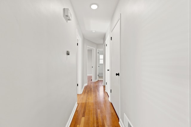 corridor with baseboards, visible vents, and light wood finished floors