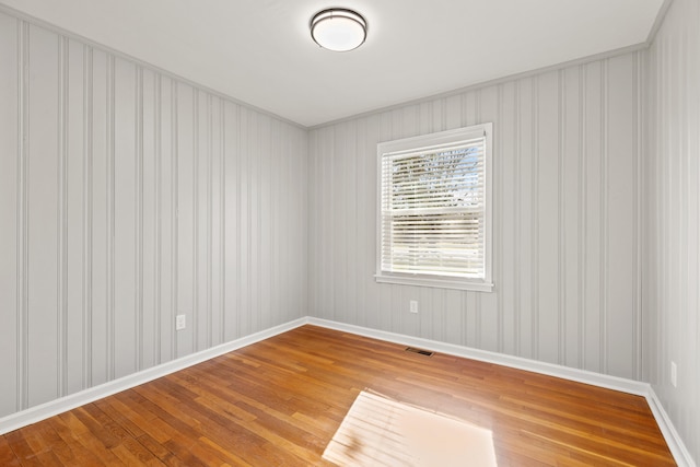 unfurnished room with visible vents, wood-type flooring, and baseboards