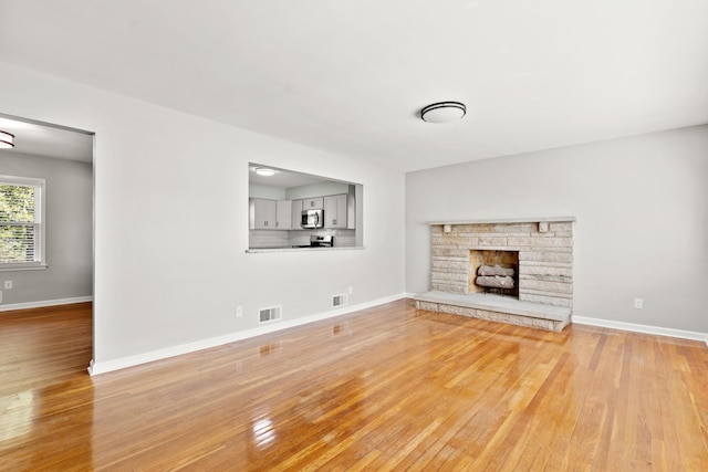 unfurnished living room with a fireplace, light wood-style floors, visible vents, and baseboards