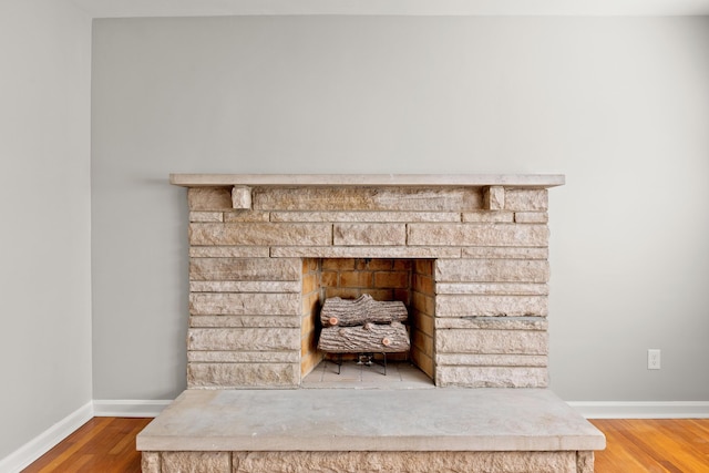 details featuring a fireplace with raised hearth, baseboards, and wood finished floors