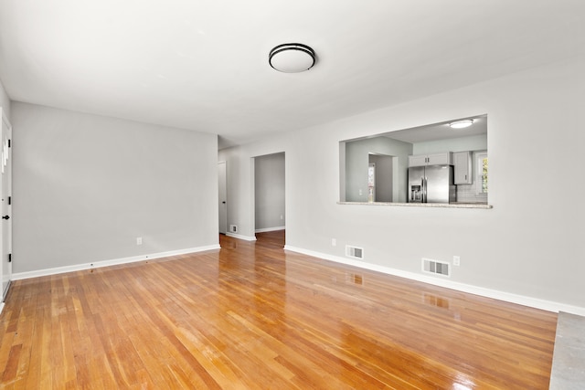 unfurnished living room with visible vents, light wood-style flooring, and baseboards