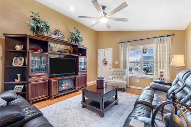 living room featuring a fireplace, a ceiling fan, baseboards, vaulted ceiling, and light wood-style floors